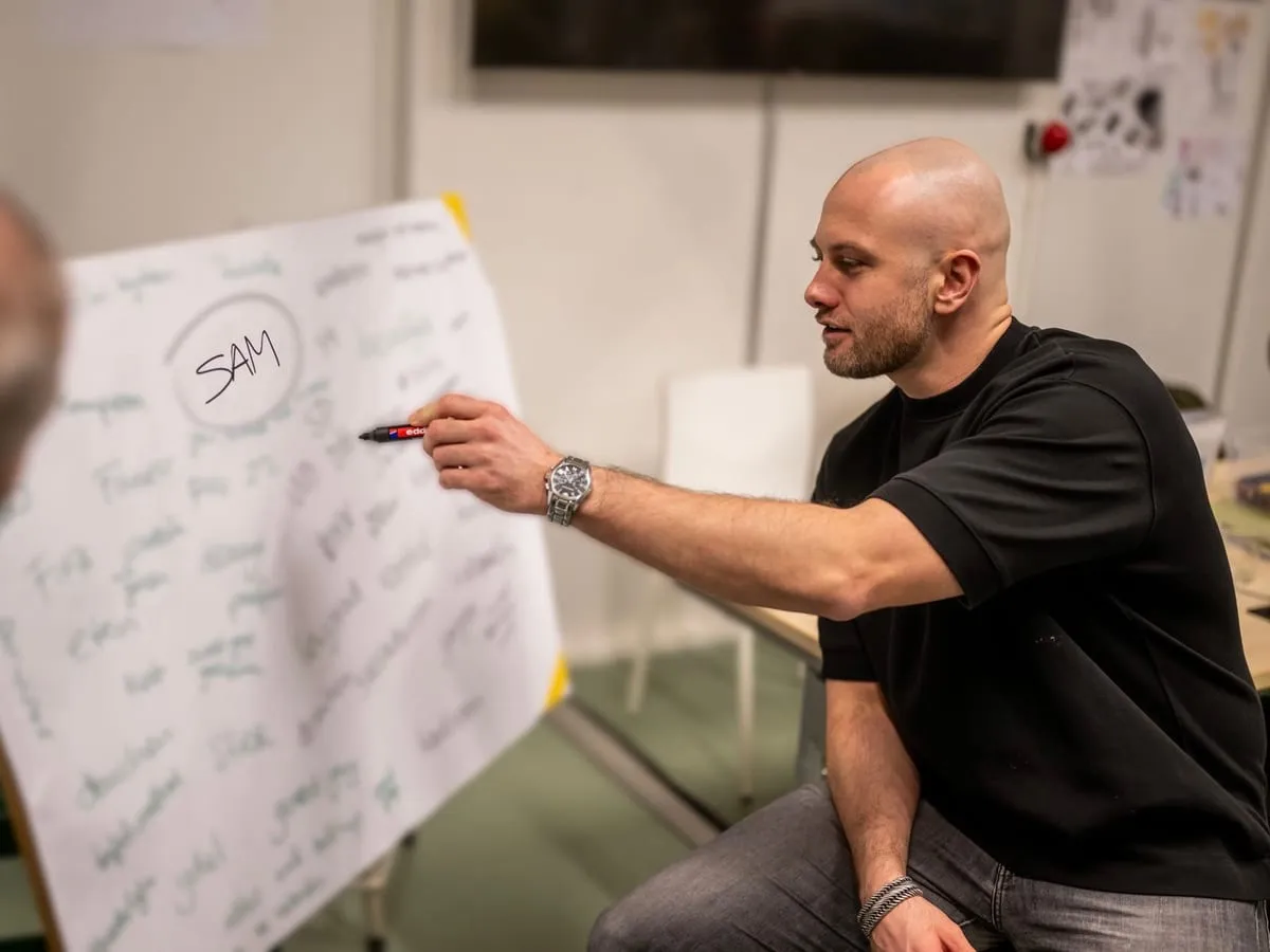 Sam wijst tijdens een gesprek naar een flipover